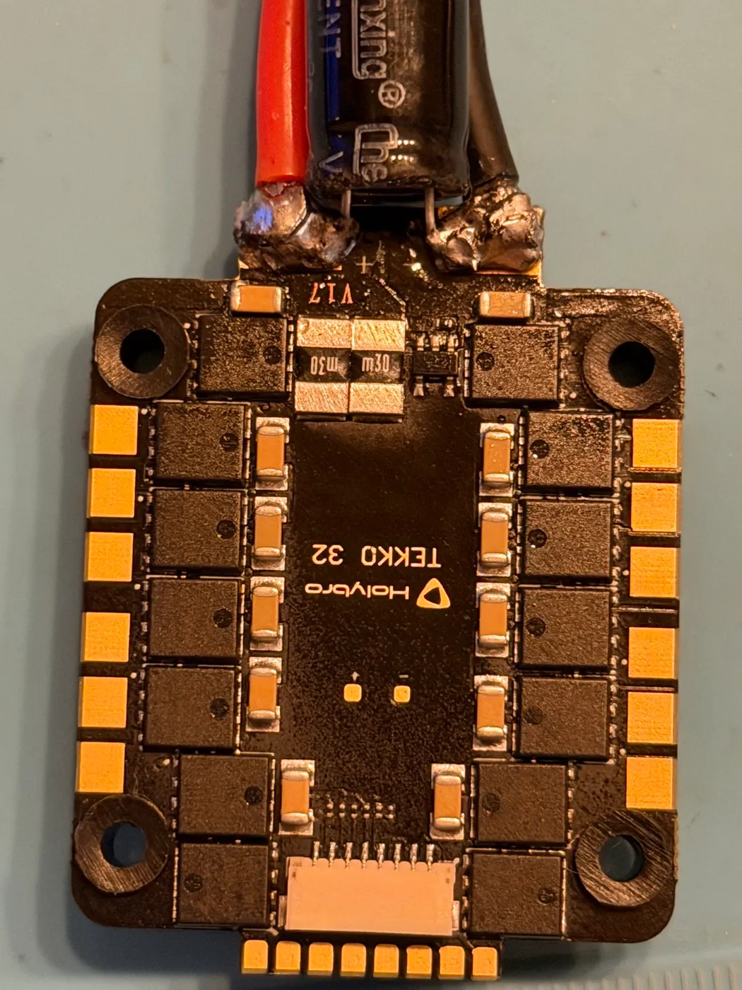 The actual Tekko32 F4 ESC from this build, top-down: XT60 pigtail and filter capacitor soldered to the B+/B− pads at the top edge, three bare motor pads at each corner, and the 8-pin FC connector at the bottom edge