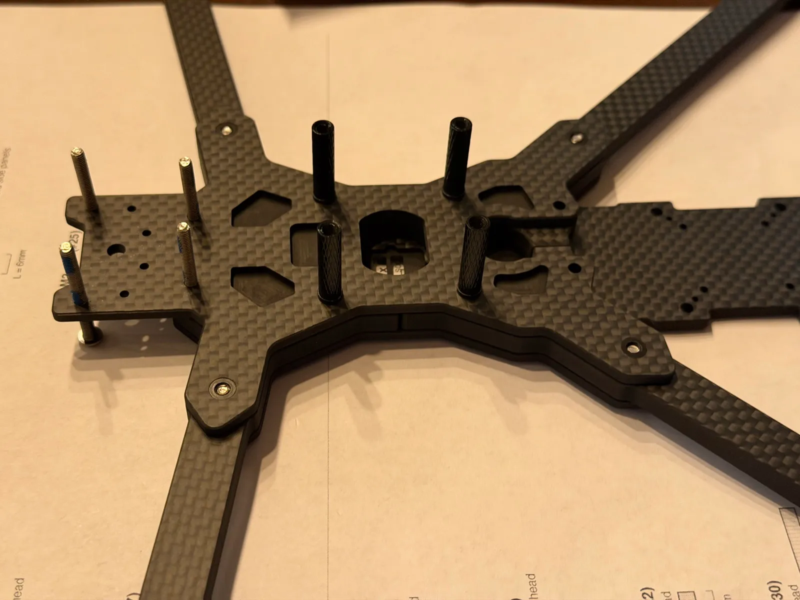 The real frame mid-Stage 3: arms clamped between the plates, four M3×20 standoffs standing on the inner-arm points, and the four nose M3×30 screws rising with threadlocker applied
